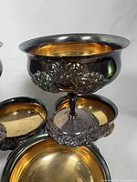 Close-up of one silver plated goblet showing ornate embossed Victorian pattern, gold-tone interior, and patina on silver exterior.