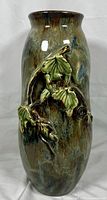 Front view of tall vintage ceramic vase showing textured raised leaf branch and swirling glaze colors.