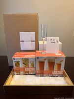 24 Adulting brand glasses including 2 boxed sets of beer and cocktail glasses, all on a gold serving tray with two white boxes behind, on a table with a beige background.