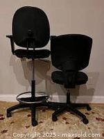 Rear view of two black office chairs, showing backrests and base with caster wheels.