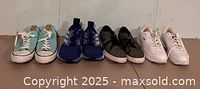 All four pairs of shoes lined up against a wall: Fila light teal sneakers, Nike Solarsoft black/grey sneakers, Adidas Continental blue sneakers, and Converse white sneakers.