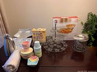 Full lot on table showing metal cupcake holders, boxed chip and dip tray, fondue warmer, ceramic plates and cups, silver carafe, and Wilton star cake pans.