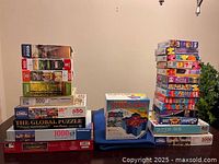 Stack of various unopened puzzles including 500 and 1000 piece puzzles with scenic and global themes