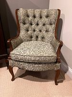 Front view of upholstered wingback chair showing tufted back, wood trim, and seat cushion with patterned fabric.