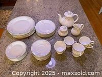 Photo of all dinnerware and tea set items showing plates, cups, saucers, teapot, sugar bowl, and creamer on countertop.