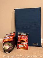 Blue Therm-a-Rest inflatable sleeping mat standing upright next to a rolled, packed Coleman Brighton tall adult sleeping bag and several packages of hand and body warmers in various pack sizes and colors.