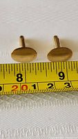 Close-up image of the oval faces of the pair of gold filled cufflinks placed next to a measuring tape indicating approximately 20mm width.