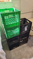 Stack of 7 plastic milk crates, 6 black and 1 green, visibly dusty and worn