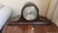 Front view of the Waterbury tambour mantle clock showing wooden casing and included winding key.