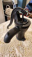 Side view of black cast iron antique well pump showing spout and handle.