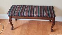 Full view of the cloth covered end of bed bench with striped cushion and wooden legs