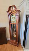 Full view of cherry-finish wooden grandfather clock with bonnet top and glass door showing pendulum and weights