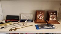 Wide view of desktop items including pens in boxes, letter openers, and a pair of Kingston wooden bookends with metal crests.