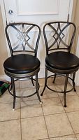 Two dark gray metal bar stools with black cushioned seats positioned on tiled floor in front of door.