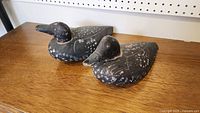 Pair of black wooden duck decoys on wooden table showing full bodies, paint chipped and worn.