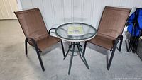 Photo of two brown mesh chairs with black metal frames positioned around a round green metal frame table with clear textured glass top.