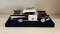 Front and left side view of the black and white metal police car model with 'Police Chief' markings sitting on a blue velvet base.