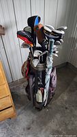 Full view of golf bag standing upright filled with an assortment of golf clubs and accessories.