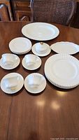 Photo of the dinner plates, cups with saucers, and oval platters arranged on a wooden table.