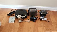 Photo showing all small appliances and kitchen tools together laid on the floor, including sandwich maker, toaster, electric chopper, pepper grinder, hand mixer, digital thermometer, and kitchen scale.