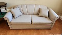 Frontal view of beige hide-a-bed sofa with two throw pillows on hardwood floor