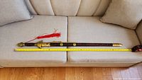 Full-length view of sword in sheath on sofa with tape measure showing approx. 40" length