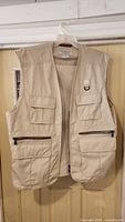 Front view of beige sleeveless vest with multiple pockets and two zippered pockets near bottom.