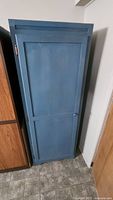 Front view of a tall, blue-painted wooden cupboard with a closed door and knob