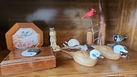 Overview of the lot showing wood carved ducks, birds on stands, decorative box with yin-yang symbol, carved figure, and framed floral and bird print in wooden frame.