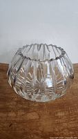 Clear crystal bowl or vase with ribbed vertical facets and scalloped rim shown from side view on wooden surface.