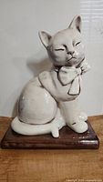 Front view of glossy white ceramic cat figurine with bow on book base. Shows overall shape and features.