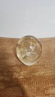 Front view of a clear and yellow tinted glass paperweight with bubble and swirl internal design on wooden surface with white background.