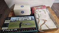 Photo showing the Tiger Woods 2000 Collector Series metal tin, HX Blue Callaway box, and Acer golf towel in plastic packaging.