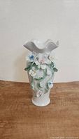 Front view of vintage white ceramic vase with scalloped rim and applied flower decorations in pastel colors.