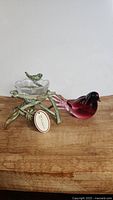 Side view of ruby red glass bird and green twig candleholder with clear flower-shaped glass candle dish and small green bird accent