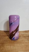 Front view of the purple cylindrical glass vase with abstract colored swirls and patterns displayed against a plain background on a wooden surface.