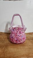 Front view of vintage hand blown glass handbag shaped vase with pink base and multicolored speckles, showing the glass handle and overall shape.