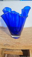 Front angle view of ruffled handkerchief cobalt blue glass vase showing curved edges and clear base.