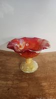 Side view showing orange and white swirled slag glass compote with ruffled edges and textured yellow slag glass base with moons and stars design.
