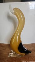Side view photo of vintage amber-yellow Murano glass goose sculpture with black tail and clear feet against white background.