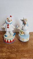 Front view of two vintage porcelain clown music box figurines on wooden surface, showing detailed colors and features