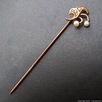 Full view of the 14k rose gold Victorian/Edwardian stick pin on a dark background highlighting its slender form and pearl embellishments.
