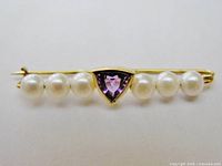 Front view of the brooch showing seven pearls and a central triangular amethyst set in gold, highlighting the symmetry and fine details.