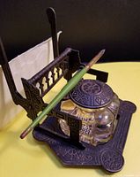 Angled view of cast iron inkwell with built-in letter holder, glass inkwell with lid, and antique dip pen resting on the holder