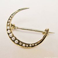 Close-up angled side view of the crescent moon brooch showing the seed pearls, gold finish, and pin closure.