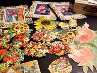 Various colorful floral paper scraps with sunflowers, roses, and butterflies along with vintage greeting card frames on a black surface.