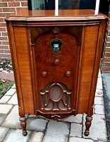 Front view of antique Roger's floor radio showing wooden cabinet with decorative carved details, analog display, three control knobs, and speaker grille.