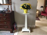 Full view of the antique white painted wooden plant stand featuring a yellow artificial flower pot on top, showing the overall condition and design.