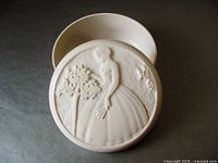 Open view of powder box showing interior and underside of lid with embossed woman and tree design.