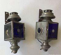 Both lanterns mounted on steel straps showing the clear and blue glass panels, red glass diamond reflector, and BRC insignia on the door.